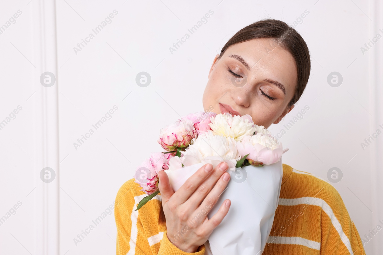 Woman with beautiful bouquet of peonies near white wall indoors, space for text Photo of Woman with beautiful bouquet of peonies near white wall indoors, space for text