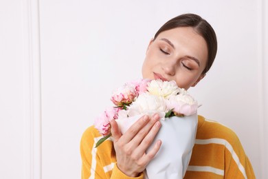 Photo of Woman with beautiful bouquet of peonies near white wall indoors, space for text