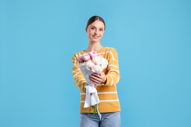 Photo of Woman with beautiful bouquet of peonies on light blue background