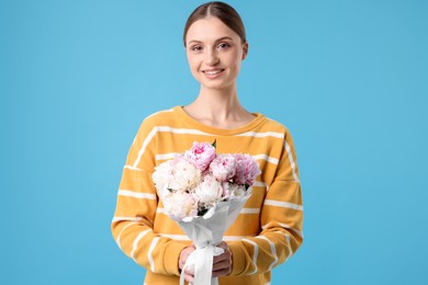 Photo of Woman with beautiful bouquet of peonies on light blue background