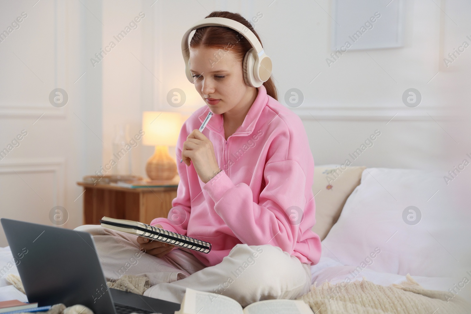 Teenage student in headphones studying on bed at home Photo of Teenage student in headphones studying on bed at home