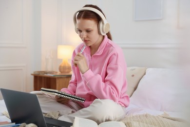 Photo of Teenage student in headphones studying on bed at home