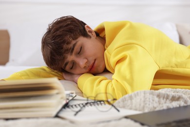 Photo of Tired teenage student sleeping near books on bed at home