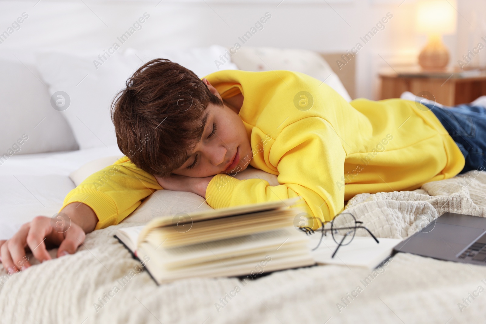 Tired teenage student sleeping near books and laptop on bed at home Photo of Tired teenage student sleeping near books and laptop on bed at home
