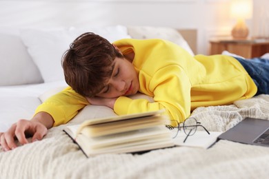 Photo of Tired teenage student sleeping near books and laptop on bed at home