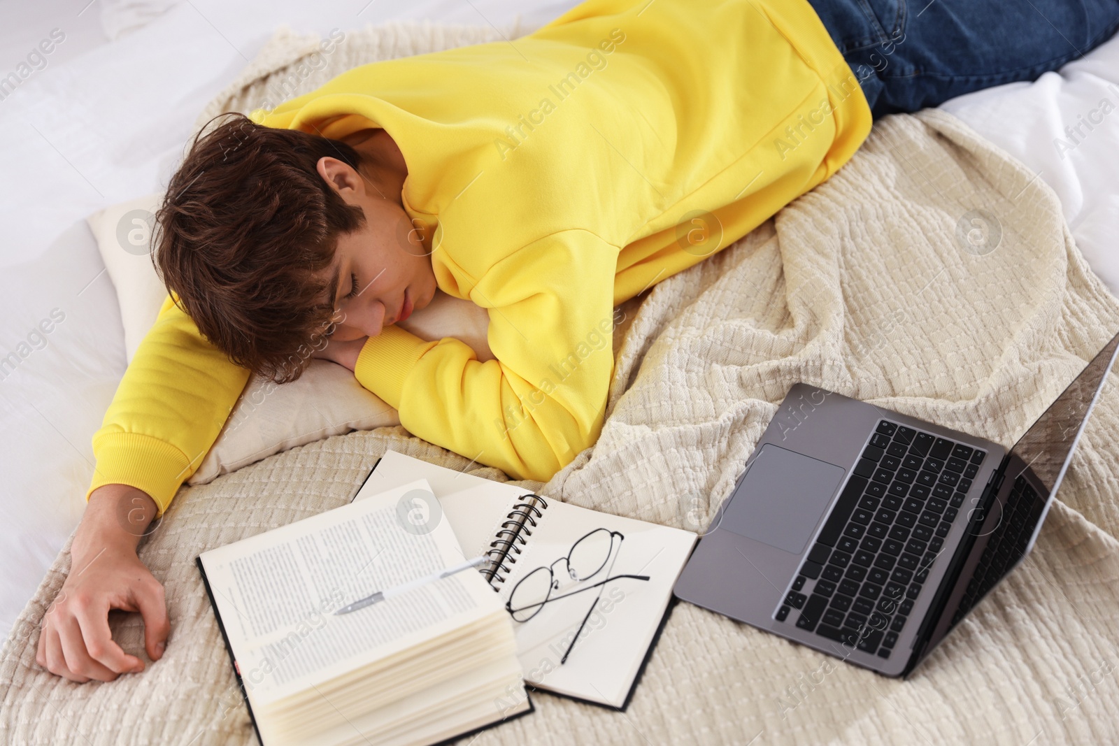 Tired teenage student sleeping near books and laptop on bed at home, above view Photo of Tired teenage student sleeping near books and laptop on bed at home, above view
