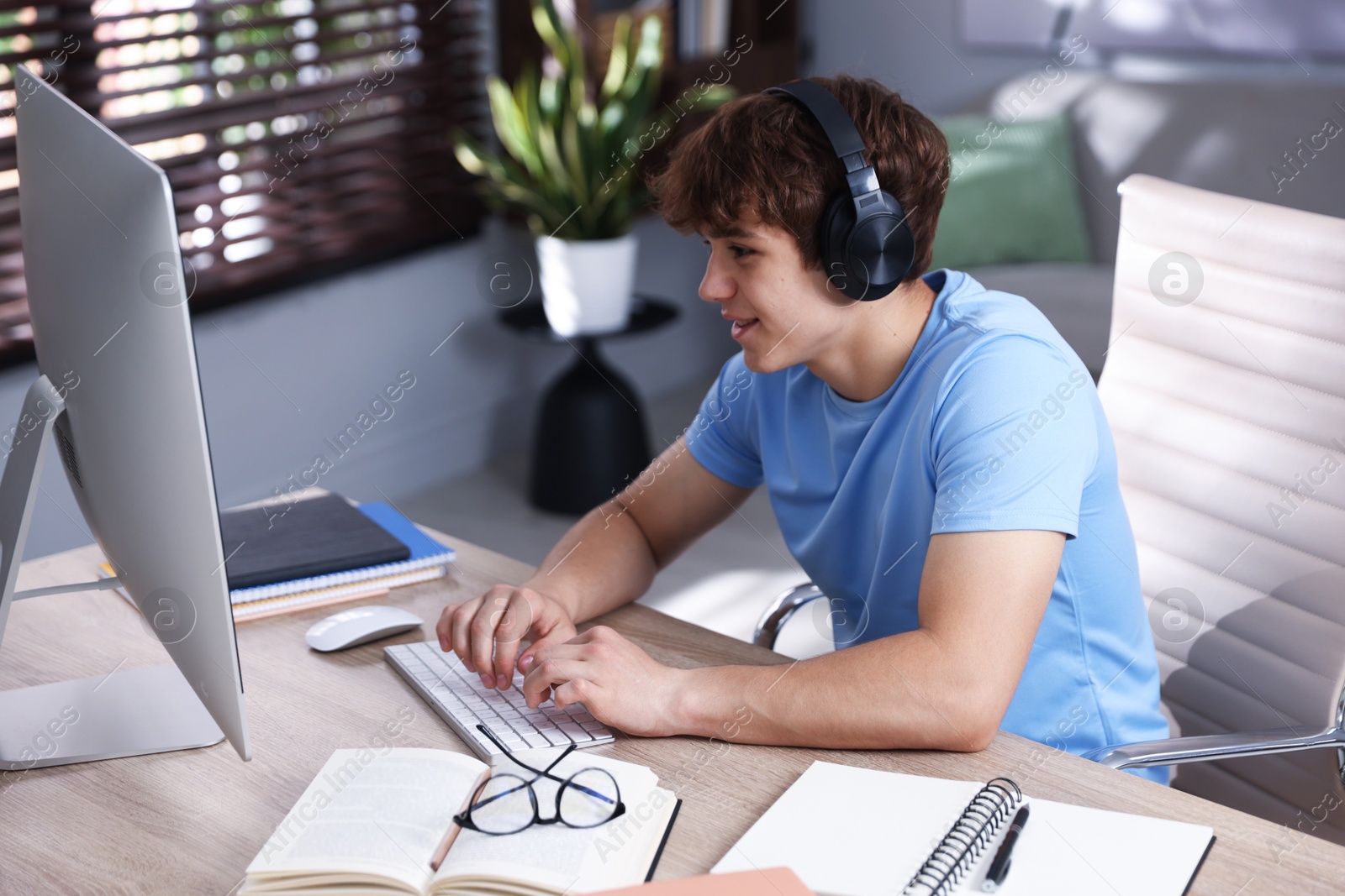 Teenage student with headphones using computer while studying at table indoors Photo of Teenage student with headphones using computer while studying at table indoors