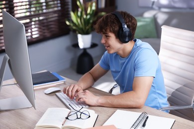 Photo of Teenage student with headphones using computer while studying at table indoors