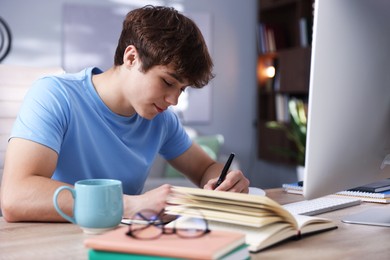 Photo of Teenage student taking notes while studying at table indoors