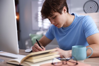 Photo of Teenage student taking notes while studying at table indoors