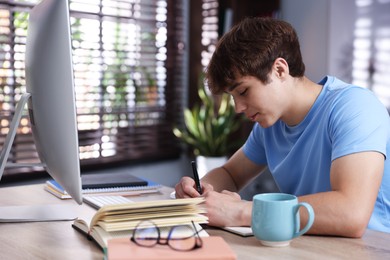 Photo of Teenage student taking notes while studying at table indoors