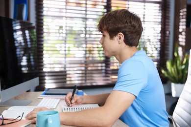 Photo of Teenage student using computer while studying at table indoors