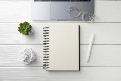Photo of Notebook, pen, glasses, laptop, crumpled paper and floral decor on white wooden table, flat lay
