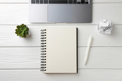 Photo of Notebook, pen, laptop, crumpled paper and floral decor on white wooden table, flat lay
