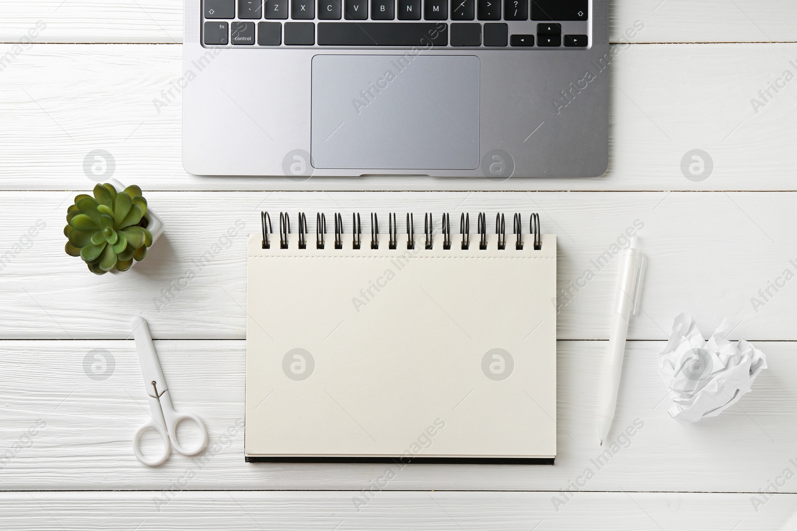Photo of Notebook, pen, laptop, crumpled paper, scissors and floral decor on white wooden table, flat lay