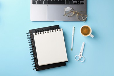 Photo of Notebooks, pen, laptop, glasses, scissors and coffee on light blue background, flat lay