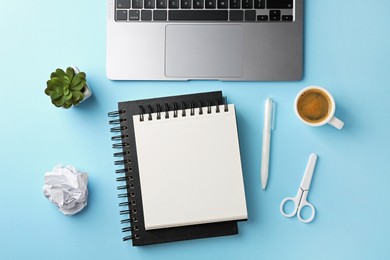 Photo of Notebooks, other stationery, laptop, glasses, crumpled paper and coffee on light blue background, flat lay