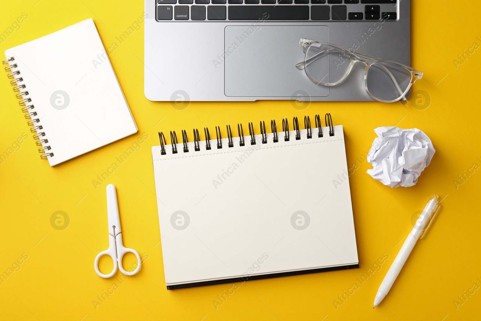 Photo of Notebooks, other stationery, glasses, crumpled paper and laptop on yellow background, flat lay