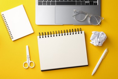 Photo of Notebooks, other stationery, glasses, crumpled paper and laptop on yellow background, flat lay