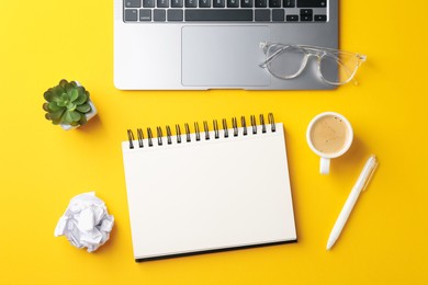 Photo of Notebook, pen, glasses, coffee, laptop and floral decor on yellow background, flat lay