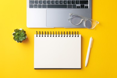 Photo of Notebook, pen, glasses, laptop and floral decor on yellow background, flat lay