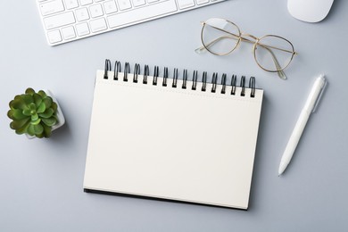 Photo of Notebook, pen, glasses, computer keyboard, mouse and floral decor on grey background, flat lay