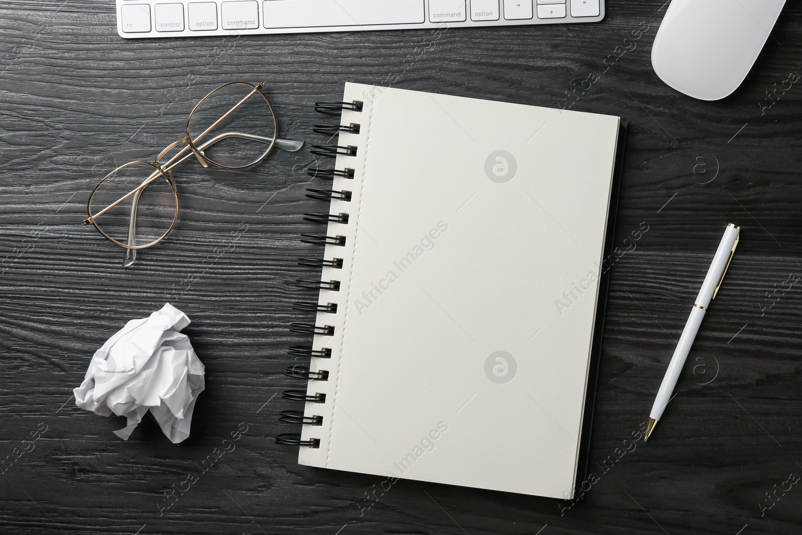 Photo of Notebook, pen, crumpled paper, glasses, computer keyboard and mouse on black wooden table, flat lay