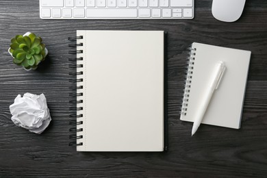 Photo of Notebooks, pen, crumpled paper, floral decor, computer keyboard and mouse on black wooden table, flat lay