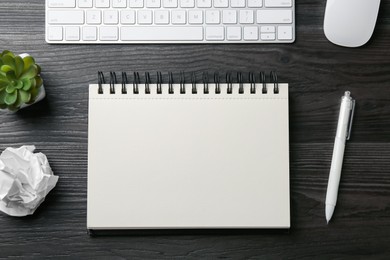 Photo of Notebook, pen, crumpled paper, floral decor, computer keyboard and mouse on black wooden table, flat lay