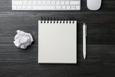 Photo of Notebook, pen, crumpled paper, computer keyboard and mouse on black wooden table, flat lay