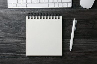 Photo of Notebook, pen, computer keyboard and mouse on black wooden table, flat lay