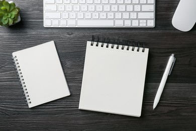 Photo of Notebooks, pen, floral decor, computer keyboard and mouse on black wooden table, flat lay