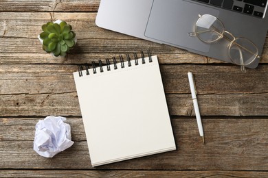 Photo of Notebook, pen, crumpled paper, glasses, floral decor and laptop on wooden table, flat lay