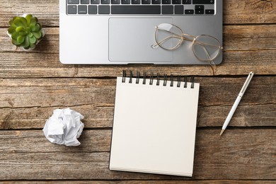 Photo of Notebook, pen, crumpled paper, glasses, floral decor and laptop on wooden table, flat lay