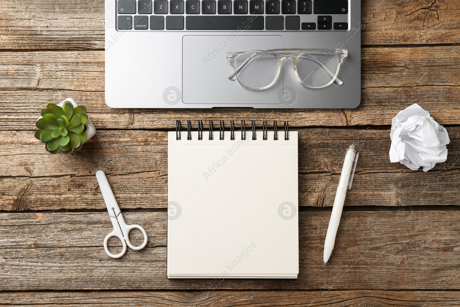 Photo of Notebook, other stationery, glasses, floral decor and laptop on wooden table, flat lay