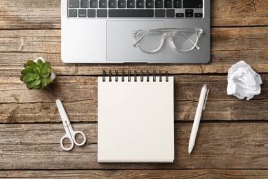 Photo of Notebook, other stationery, glasses, floral decor and laptop on wooden table, flat lay