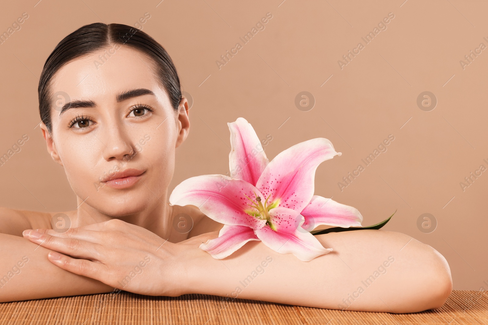 Beautiful woman after spa treatment with lily flower at bamboo table on beige background Photo of Beautiful woman after spa treatment with lily flower at bamboo table on beige background