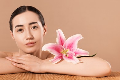Photo of Beautiful woman after spa treatment with lily flower at bamboo table on beige background