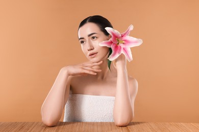 Photo of Beautiful woman after spa treatment with lily flower at bamboo table on beige background