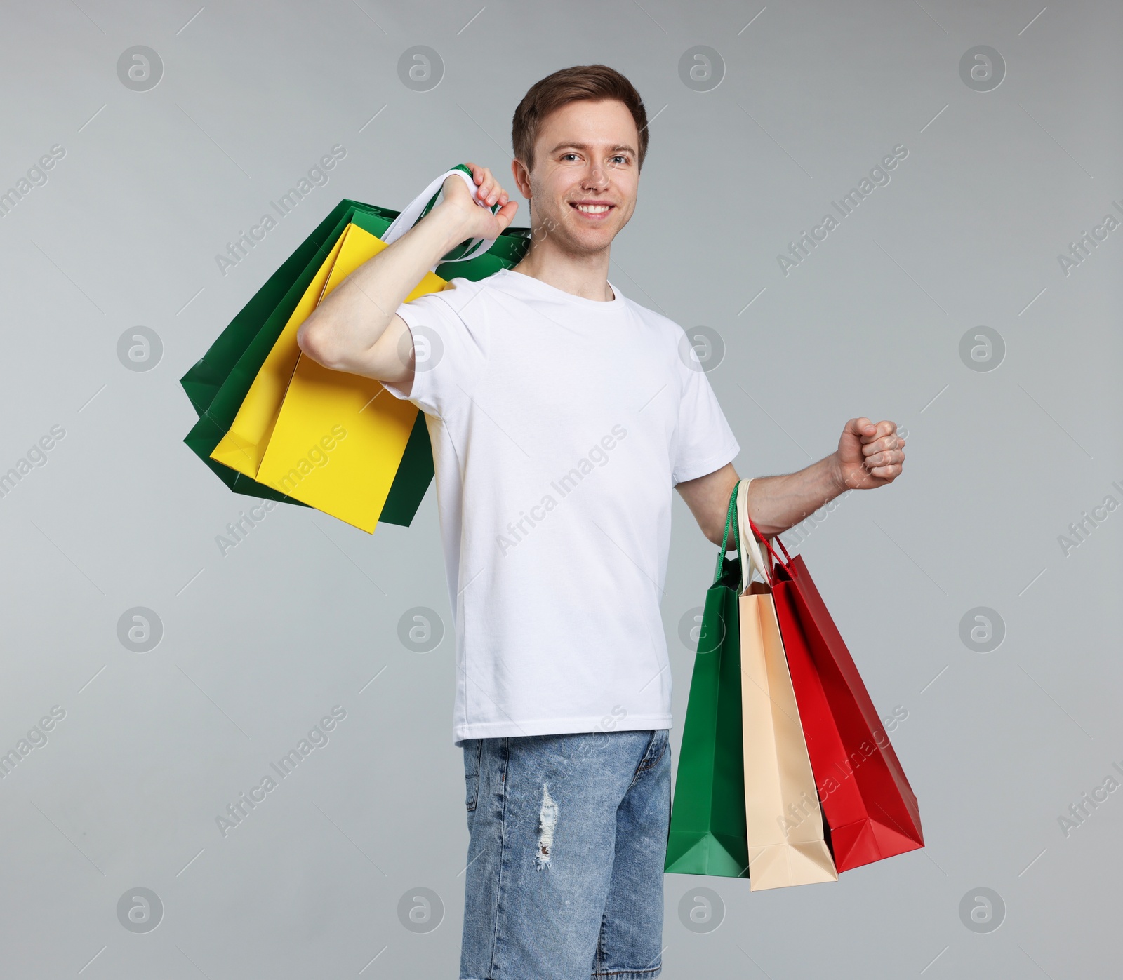 Cheerful man with shopping bags on light grey background Photo of Cheerful man with shopping bags on light grey background