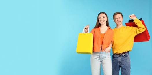 Photo of Happy couple with shopping bags on light blue background