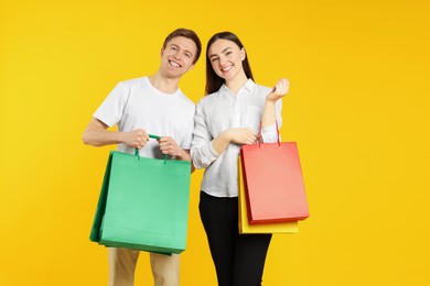 Photo of Happy couple with shopping bags on yellow background