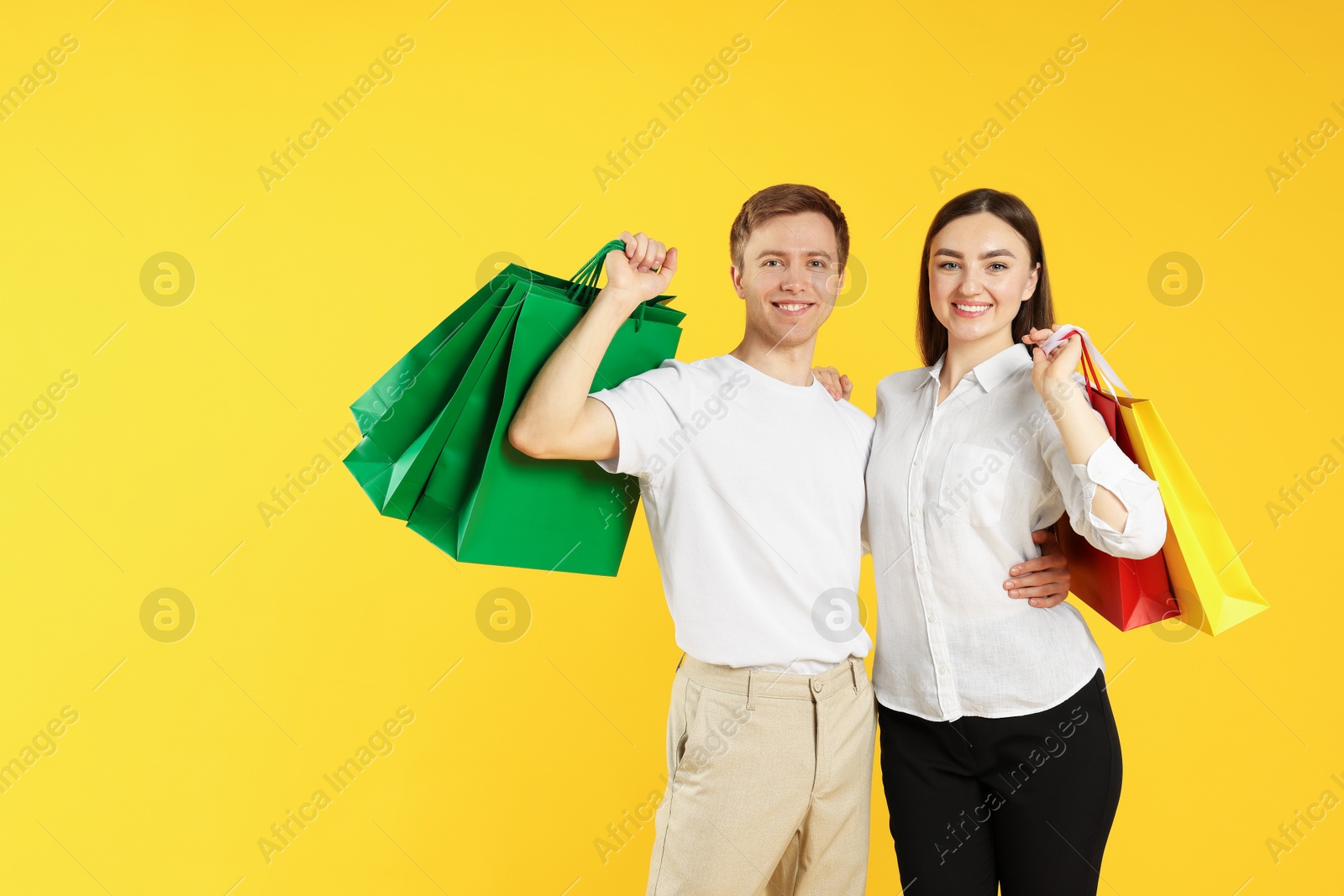 Happy couple with shopping bags on yellow background Photo of Happy couple with shopping bags on yellow background