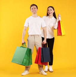 Photo of Happy couple with shopping bags on yellow background