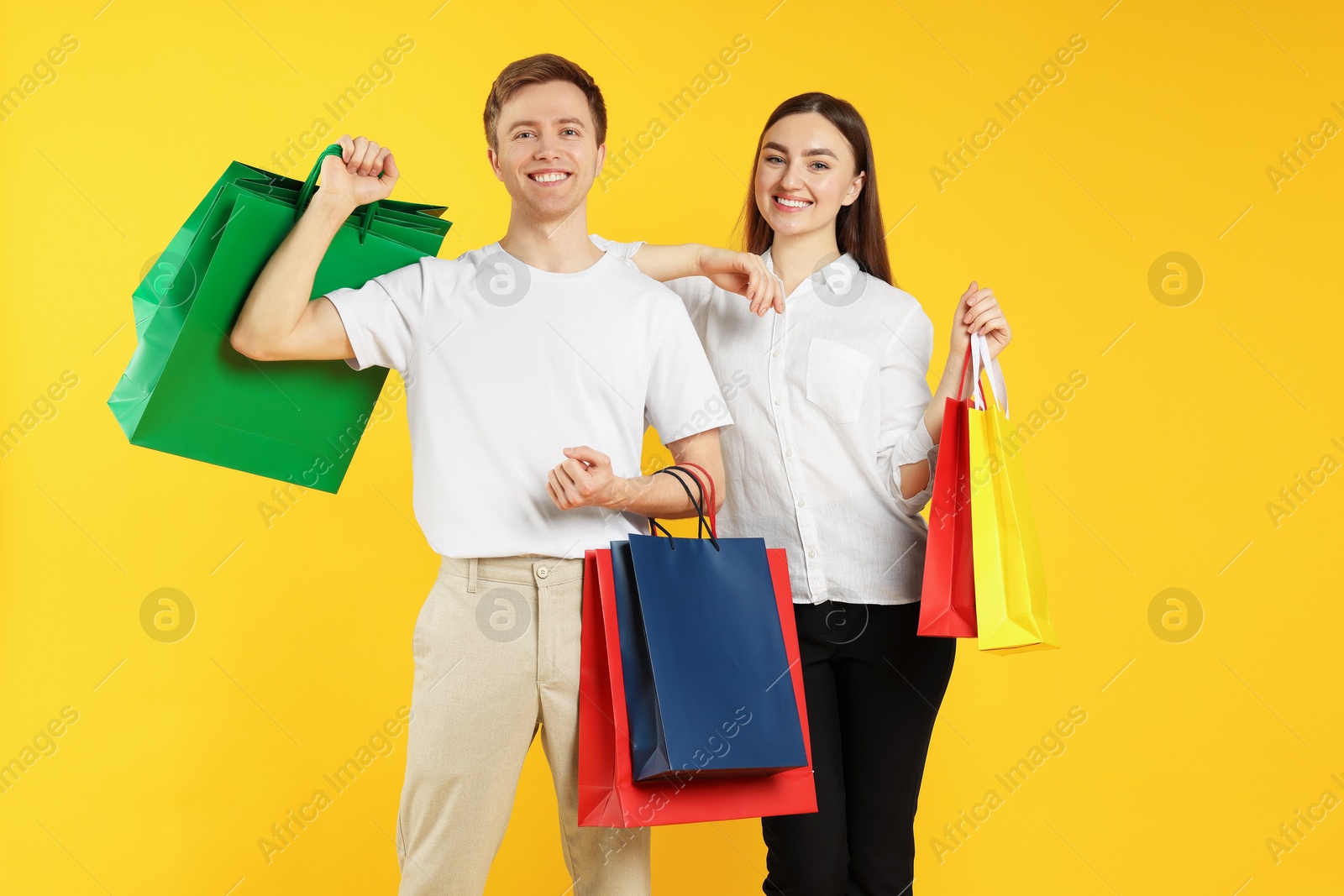 Happy couple with shopping bags on yellow background Photo of Happy couple with shopping bags on yellow background