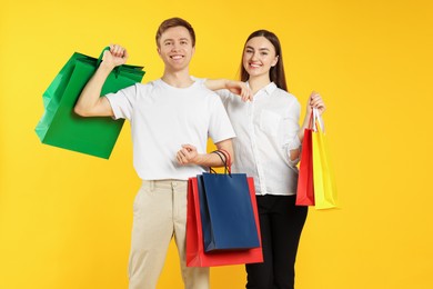 Photo of Happy couple with shopping bags on yellow background