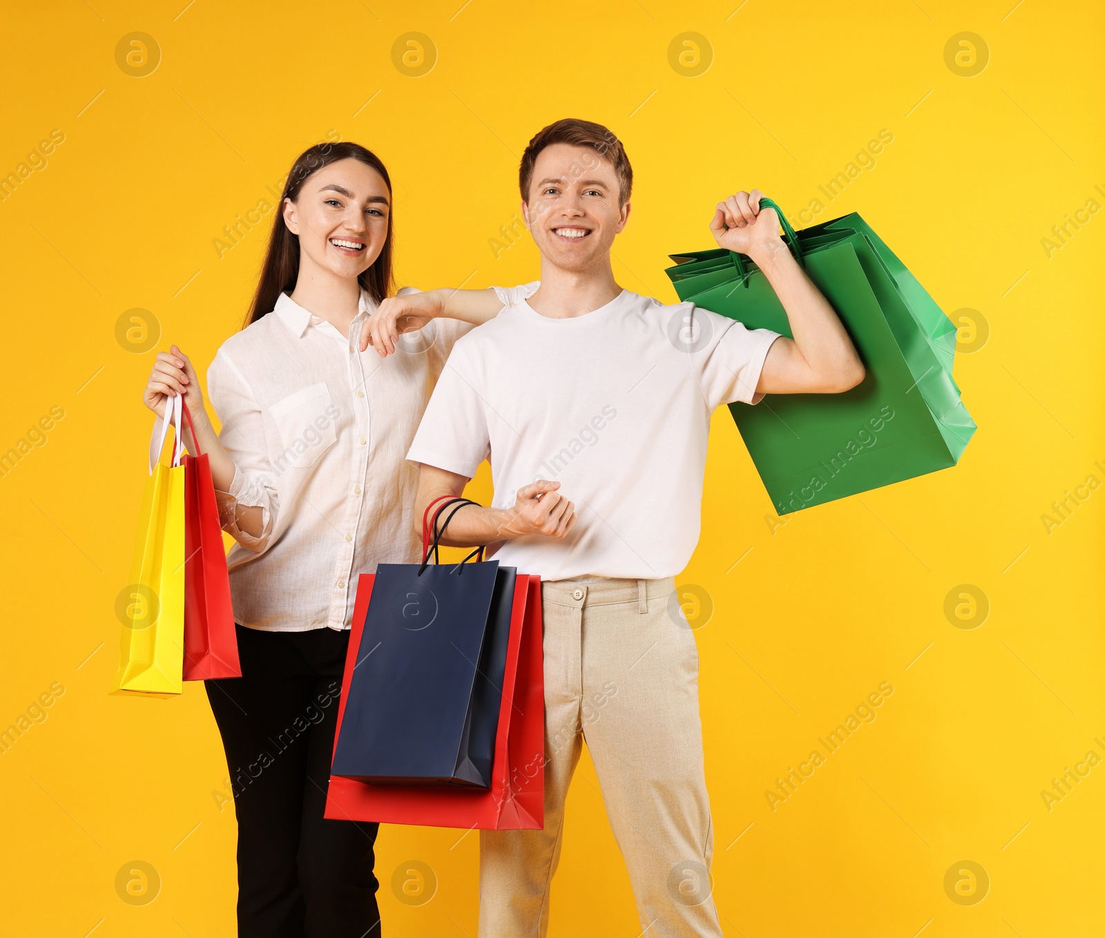 Happy couple with shopping bags on yellow background Photo of Happy couple with shopping bags on yellow background