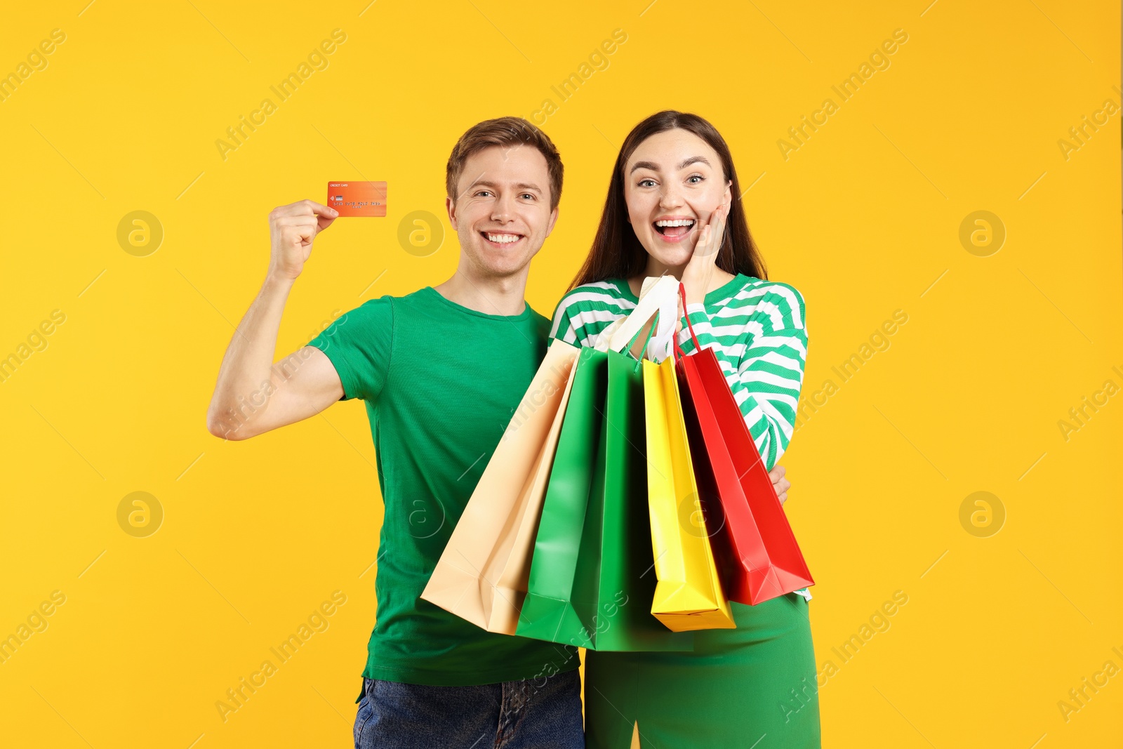 Happy couple with credit card and shopping bags on yellow background Photo of Happy couple with credit card and shopping bags on yellow background