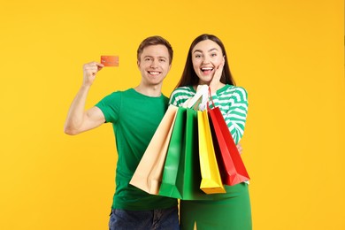 Photo of Happy couple with credit card and shopping bags on yellow background