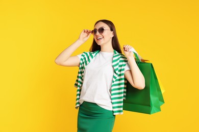 Photo of Positive woman with shopping bags on yellow background